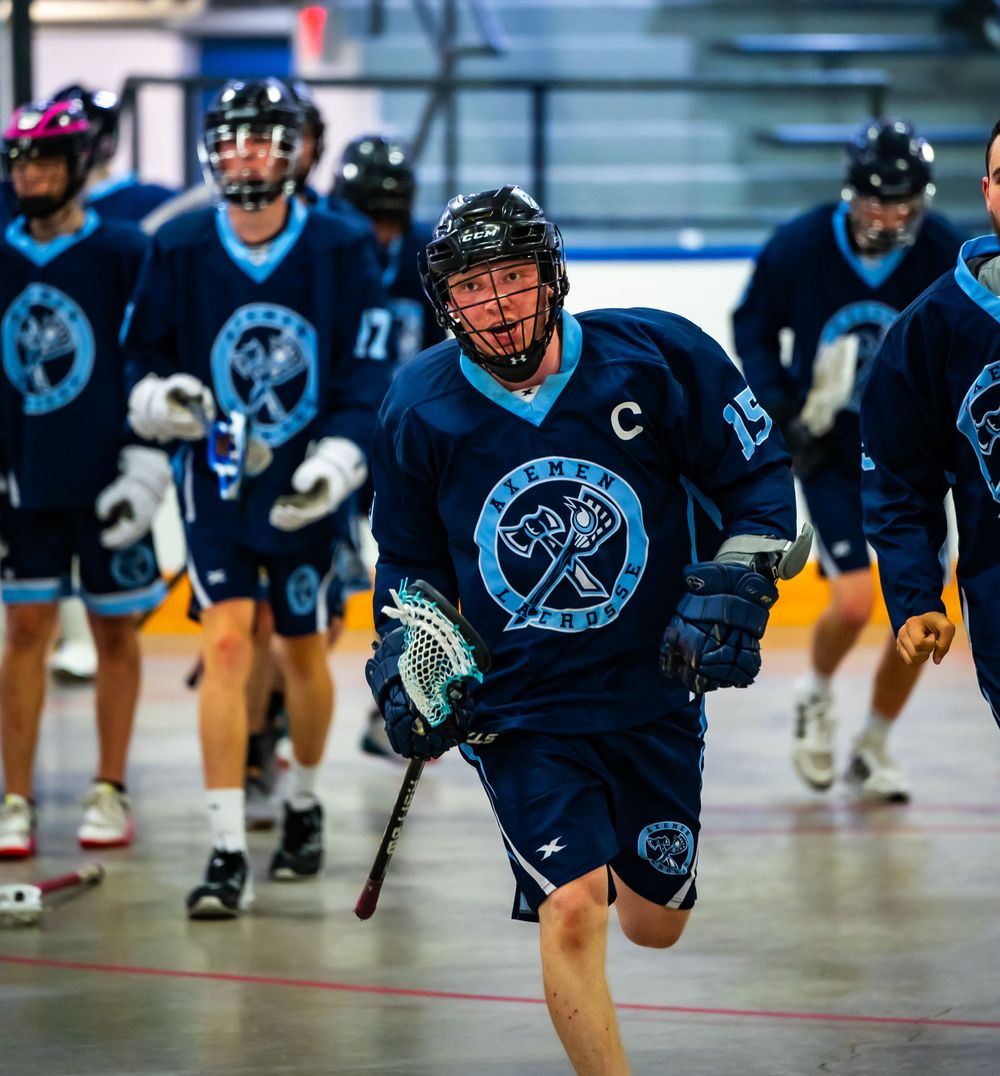 Lacrosse player in navy blue uniform with team logo running on indoor court.