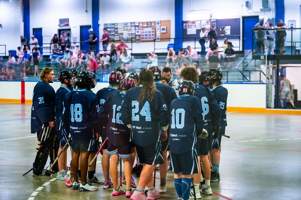 Team of lacrosse players in dark uniforms gathering on indoor court.