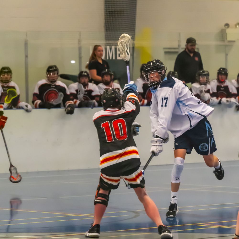 Two opposing lacrosse players compete for the ball during an indoor game.