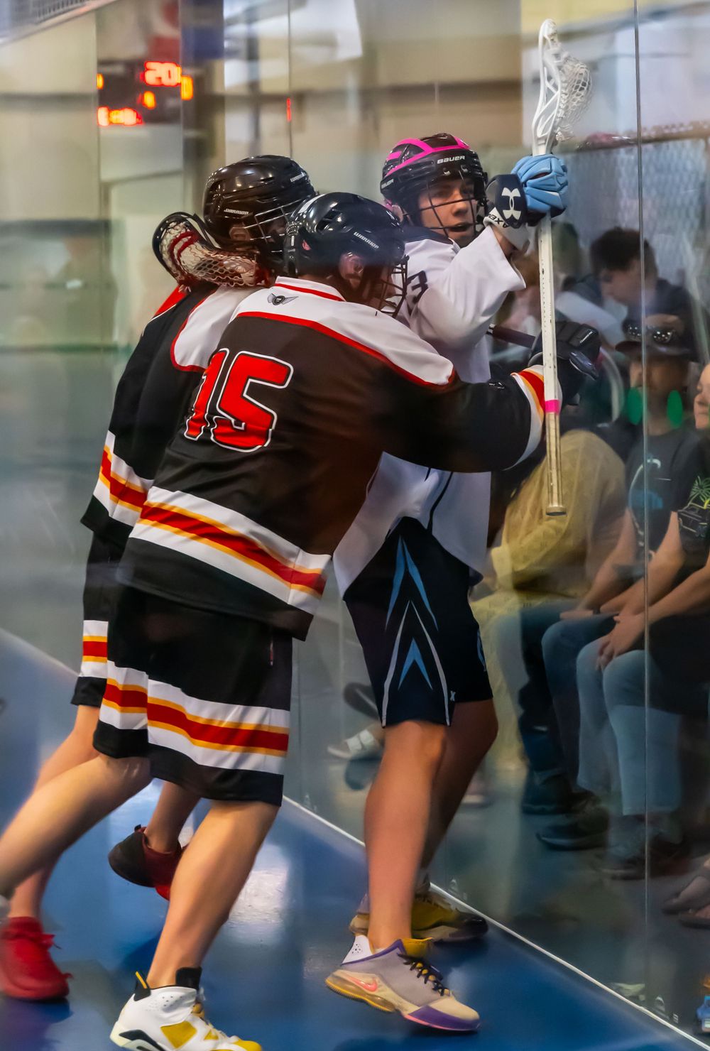 Two lacrosse players battle against the boards during an intense indoor match.