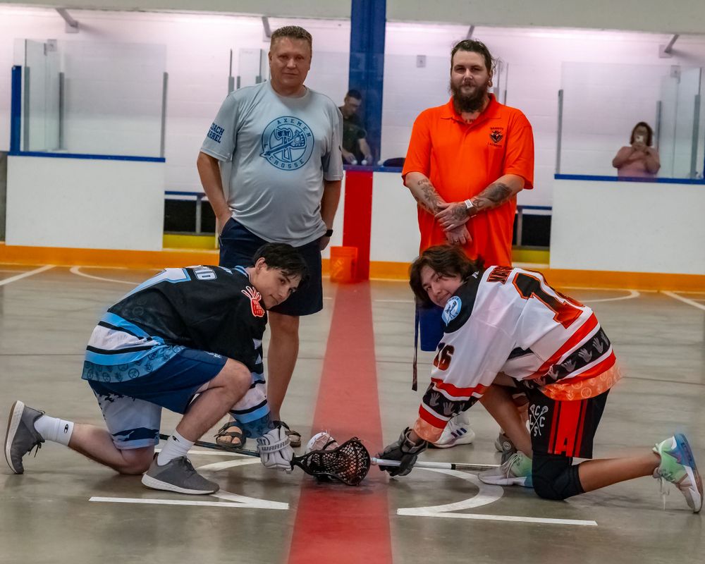 Two youth players face off in indoor floor hockey game as coaches watch.