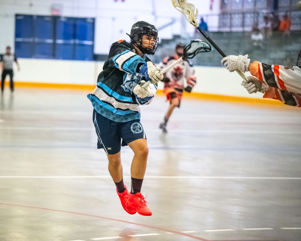 A player in blue jersey takes a shot during an indoor box lacrosse game.