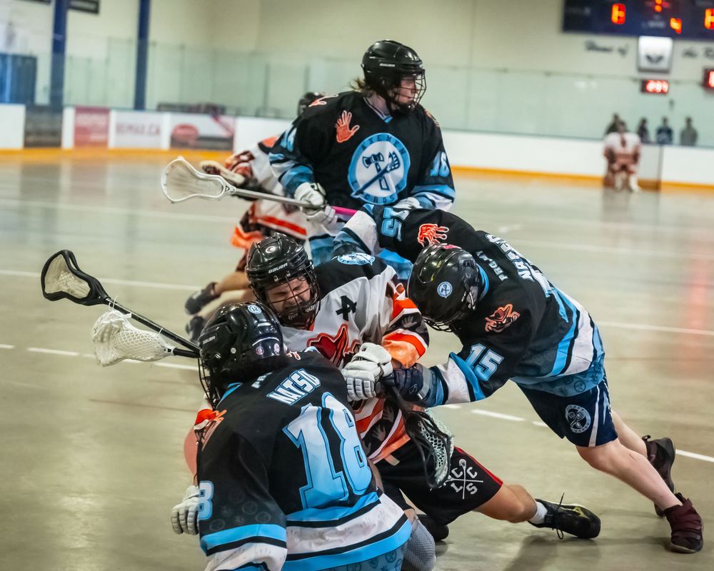 Multiple players scramble for the ball during an intense box lacrosse match.