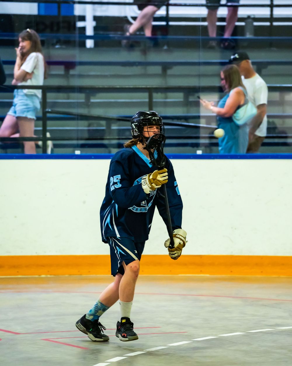 A player in blue uniform prepares for action during an indoor lacrosse game.