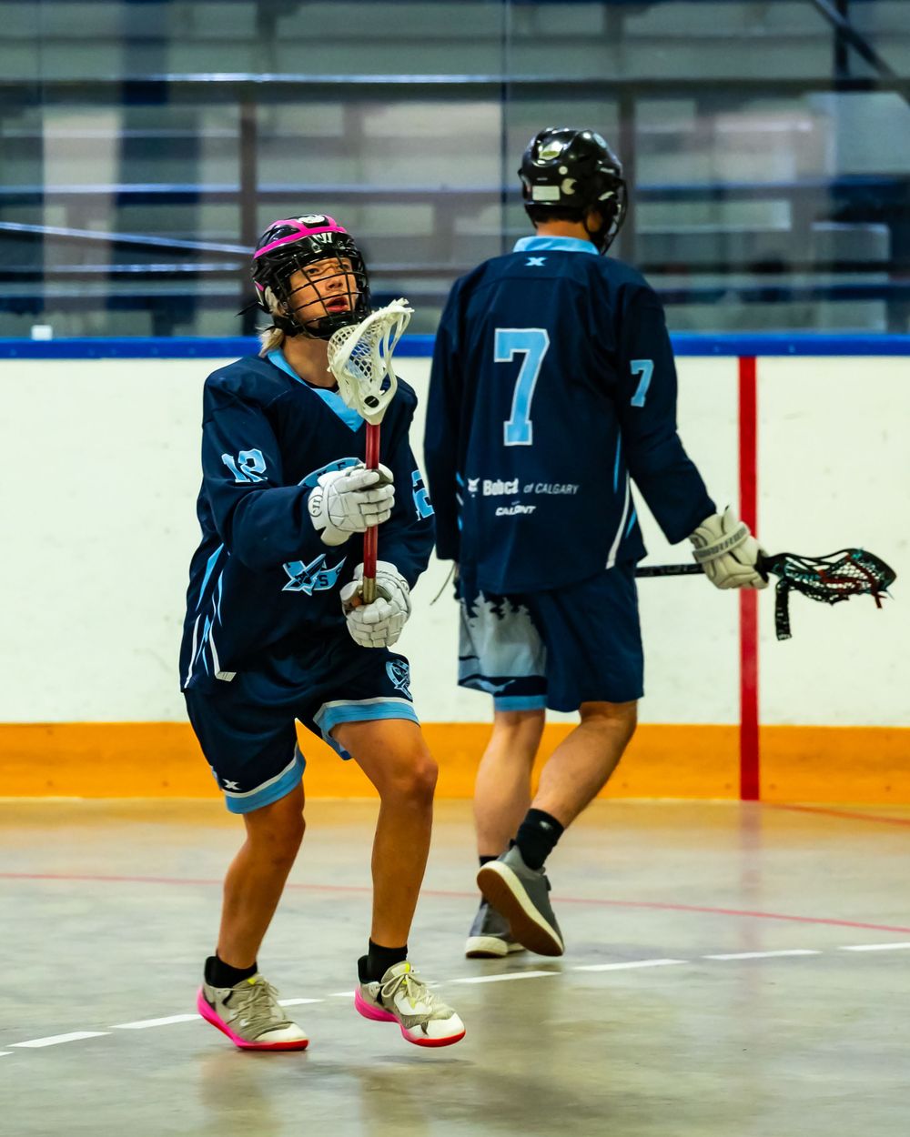 Two teammates in blue jerseys communicate during a box lacrosse match.