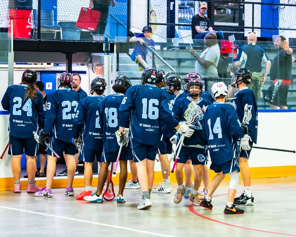Indoor lacrosse team in navy blue jerseys huddles together during a game.