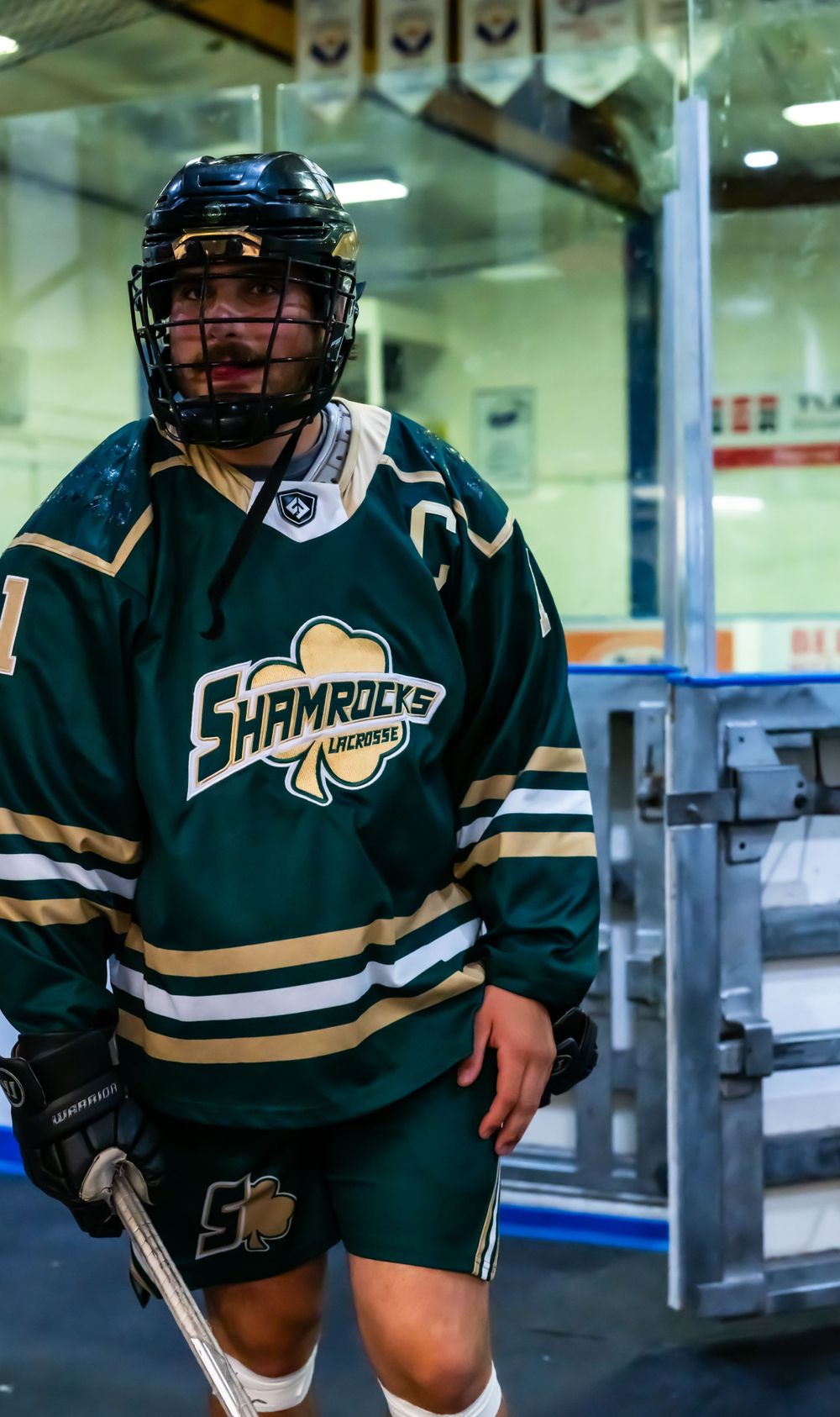 Ice hockey player wearing a green Shamrocks jersey with protective gear and helmet standing in an arena.