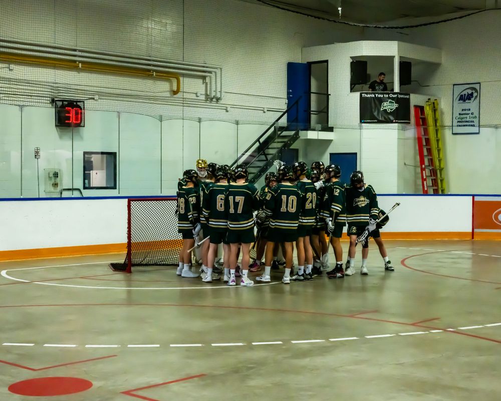 Hockey team in green jerseys huddling together on the rink before a game.