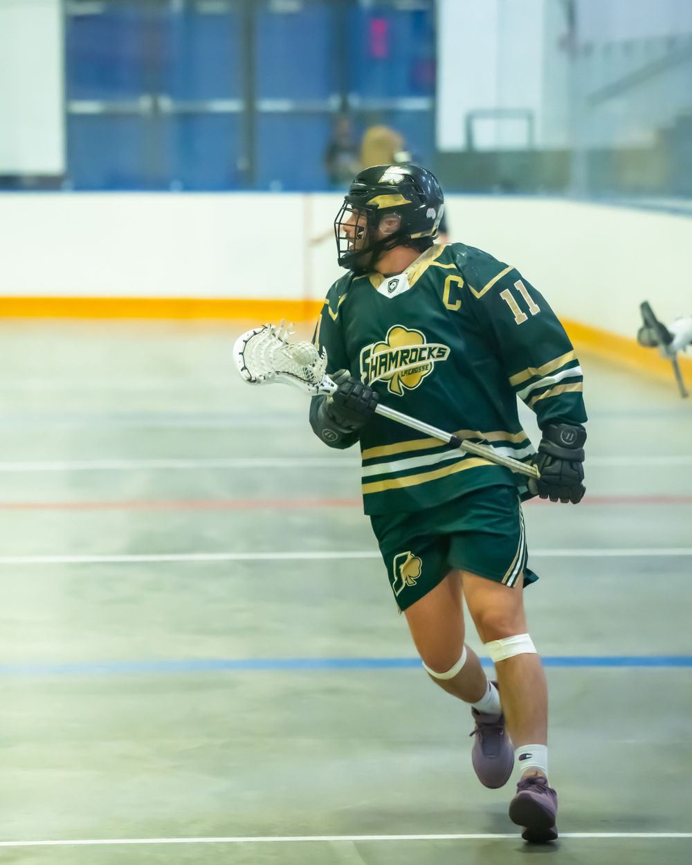 Hockey player in green Shamrocks uniform running with a stick during indoor game.