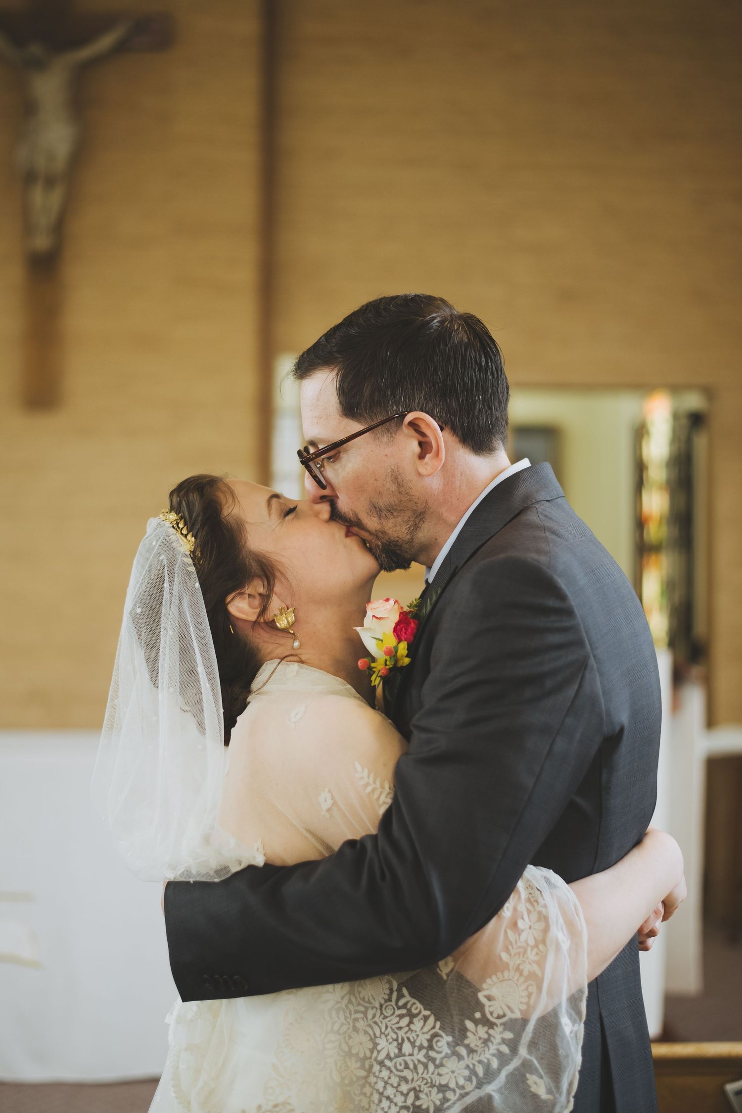 Romantic wedding kiss between newlyweds in front of a church altar with crucifix.