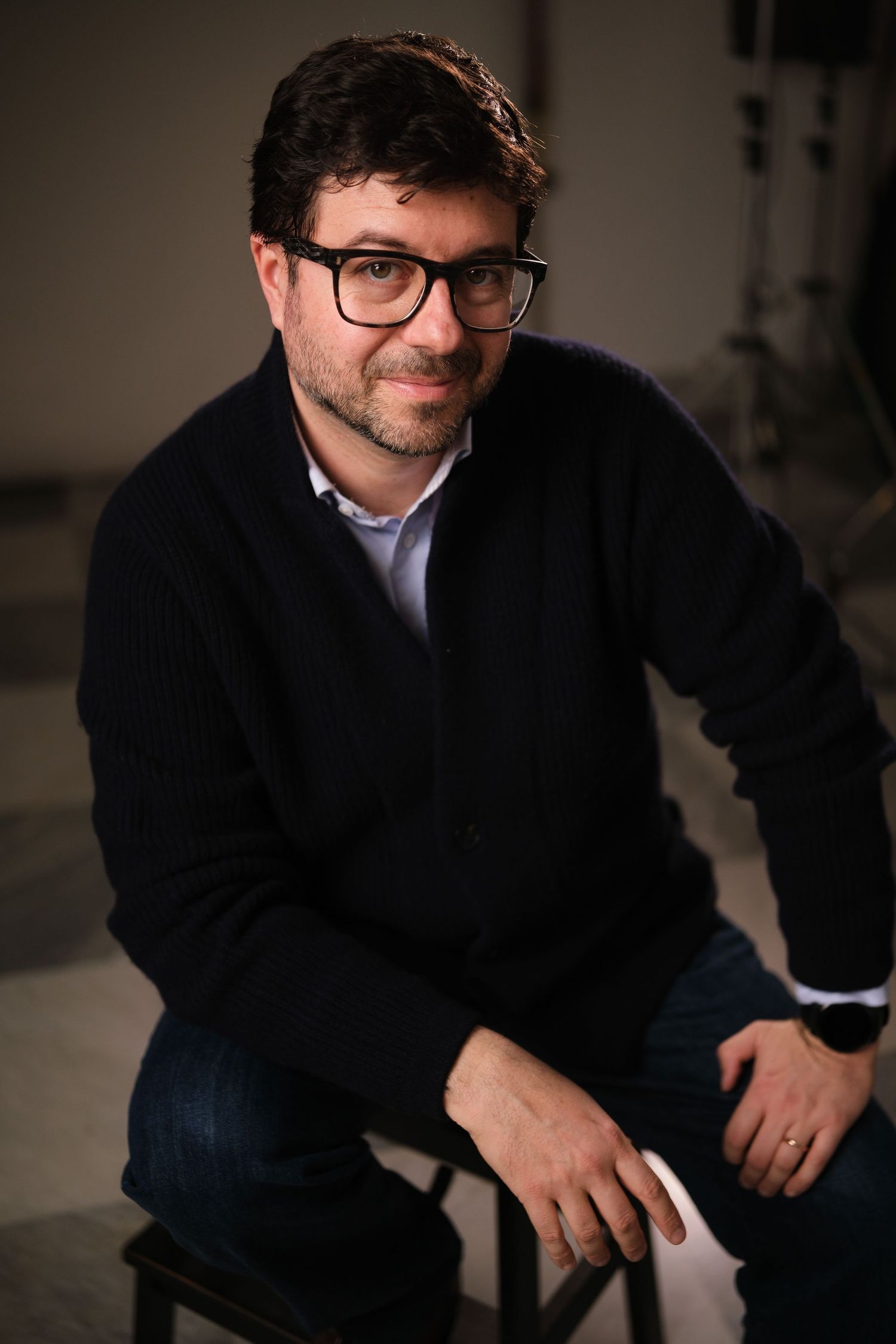 Professional headshots of a man in glasses and black coat showing different expressions.
