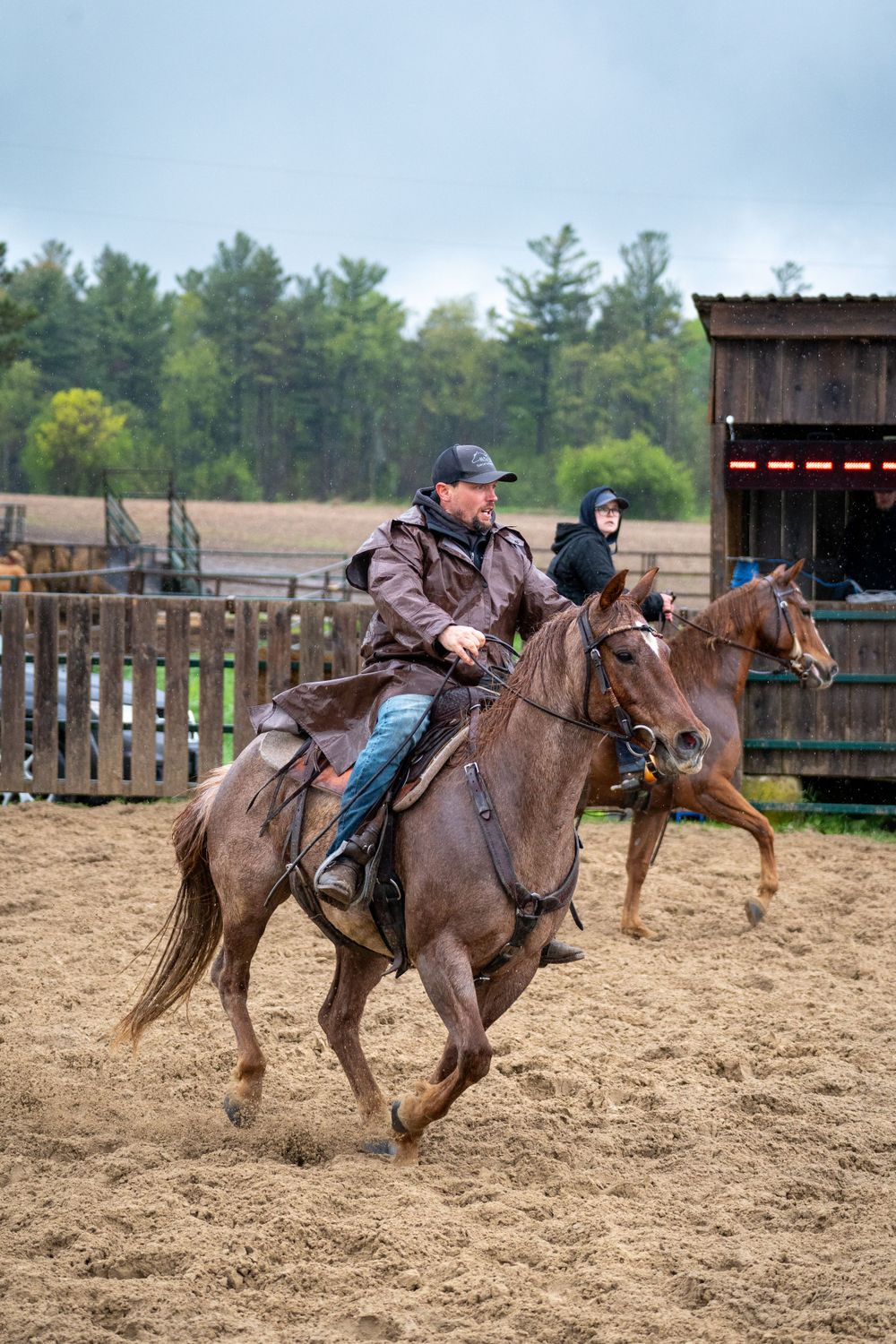 Riders on horseback compete in ranch sorting competition in muddy arena.