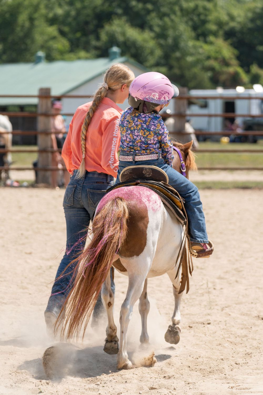 Young rider practices horseback riding on a paint pony while being supervised in an outdoor arena.