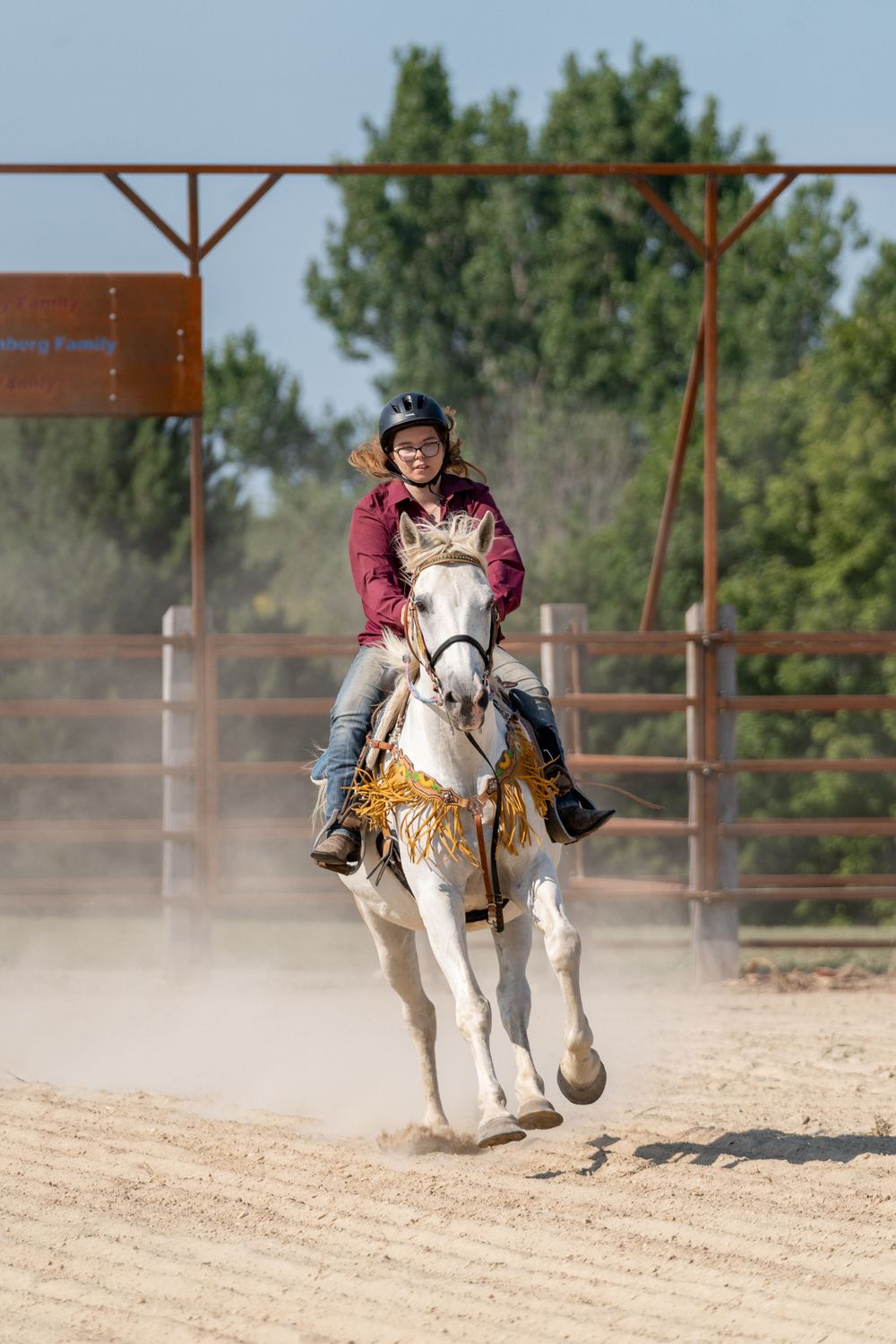A white horse gallops through a dusty arena during a riding competition.
