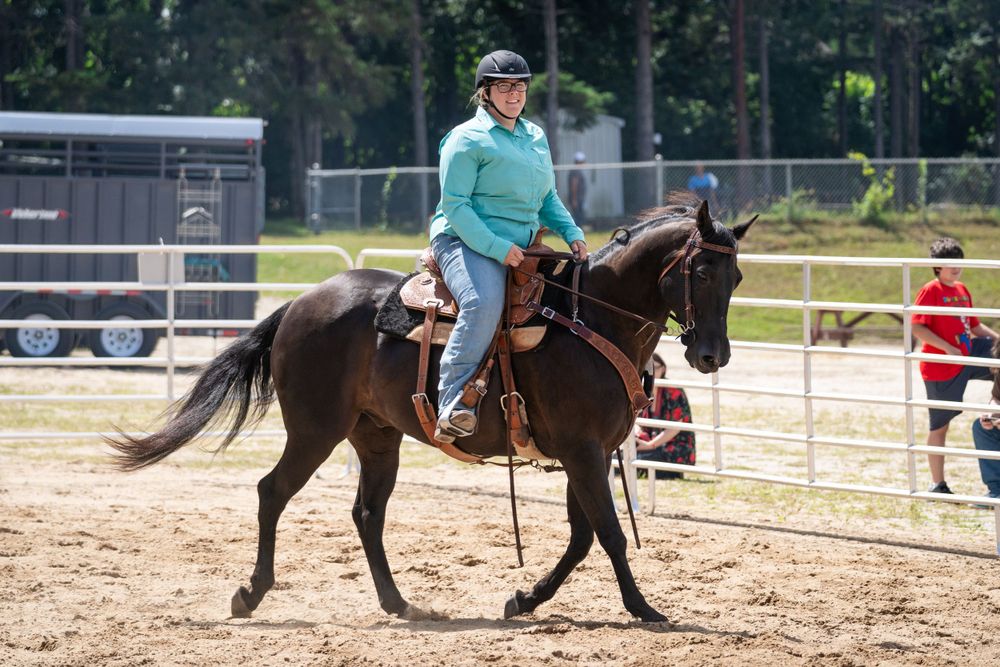 A rider in turquoise attire guides a dark horse through an outdoor arena during an equestrian event.