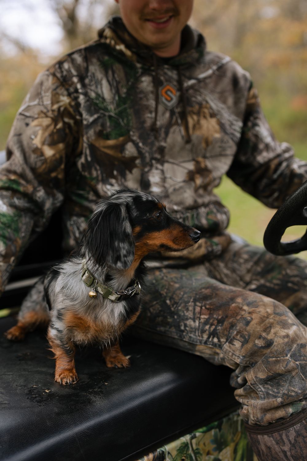 weiner dog sitting on seat next to a man in camouflage clothing driving an offroad vehicle
