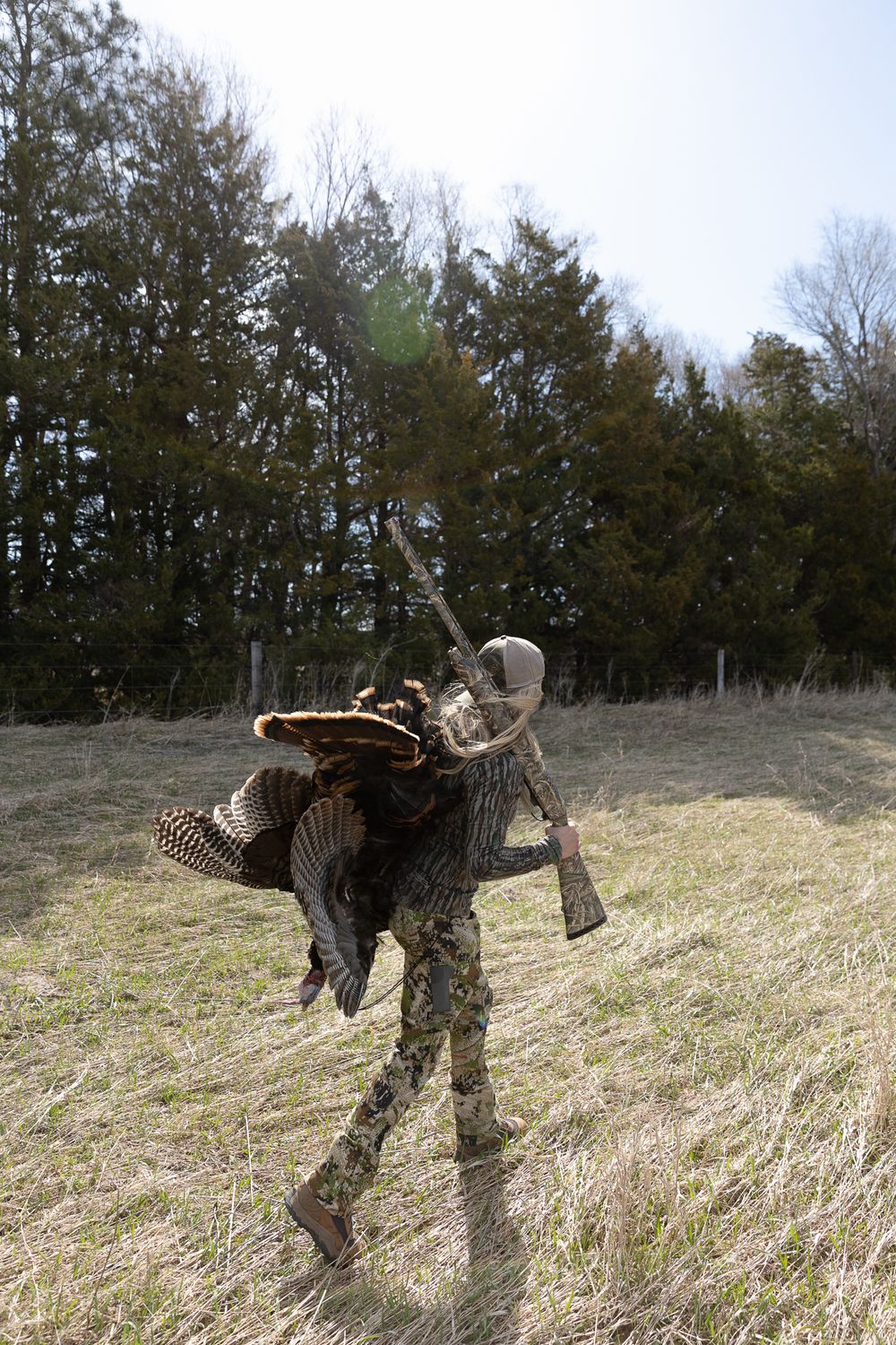 woman walking in camo clothing holding shotgun and turkey over shoulder
