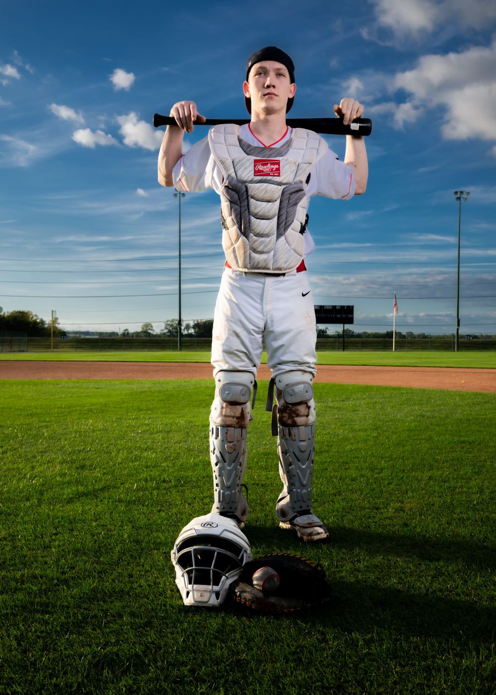 A baseball player in white uniform poses with bat on field under blue sky.