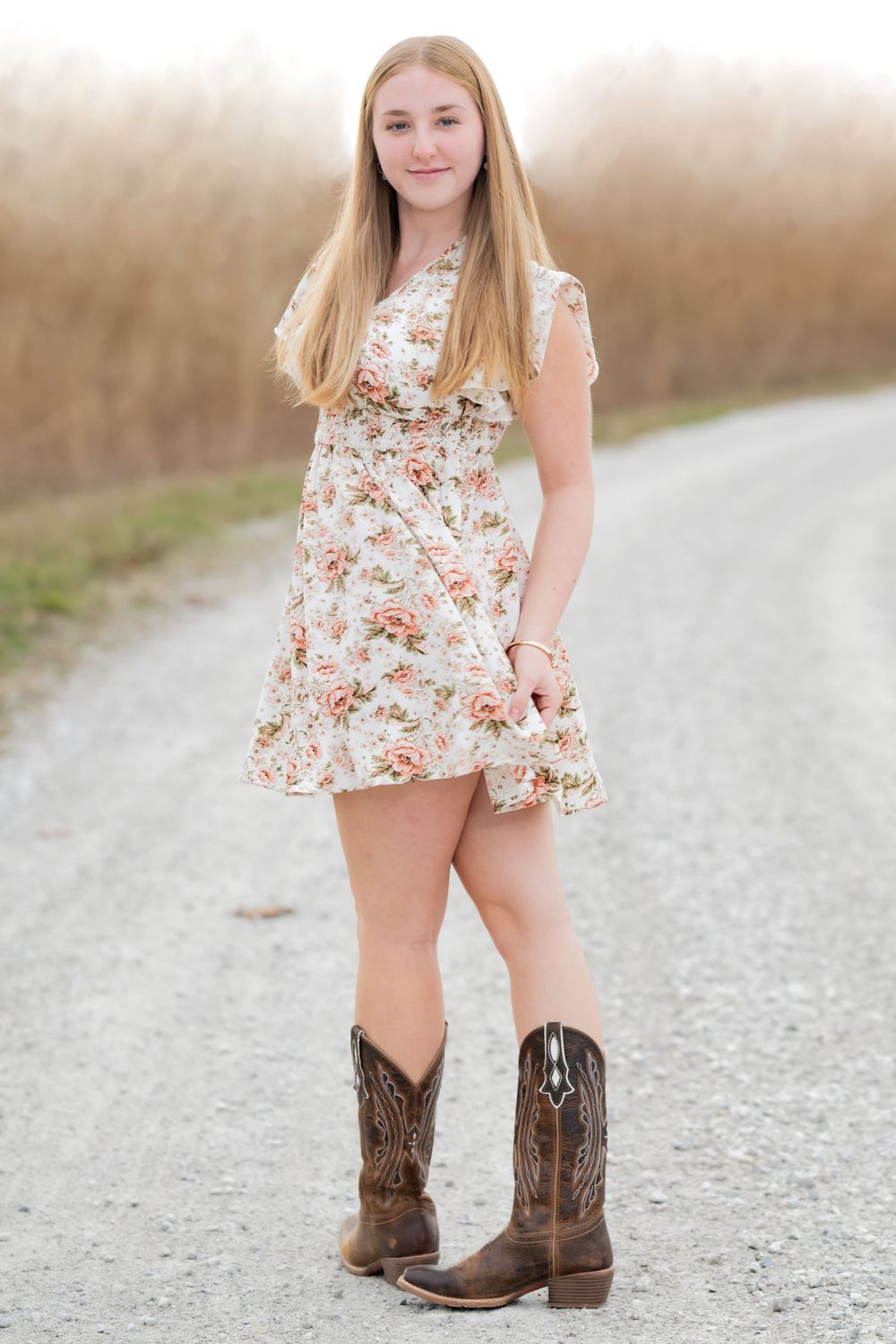 Country style portrait in floral dress and cowboy boots on gravel road.