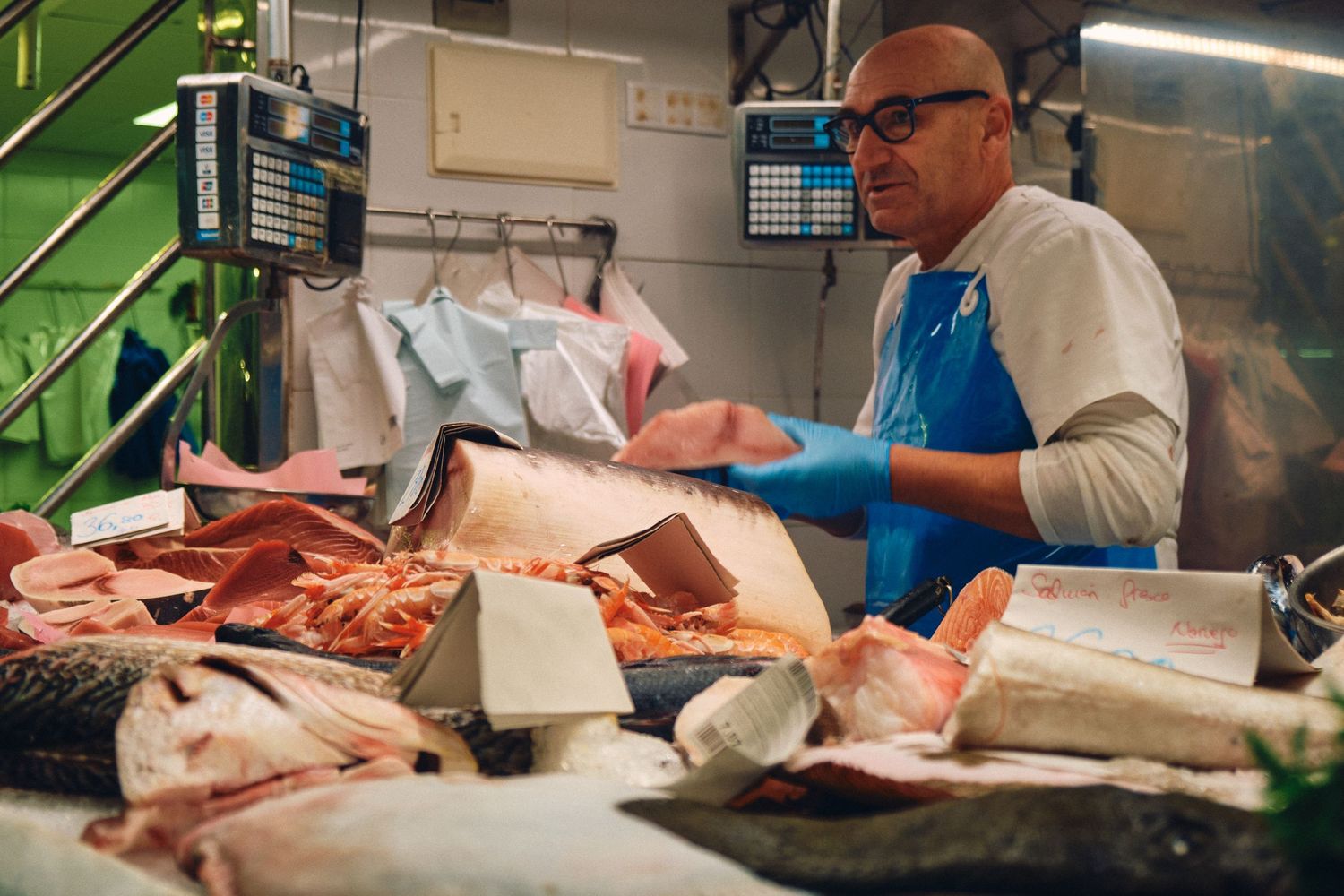 Fishmonger in blue apron preparing fresh seafood at market counter.