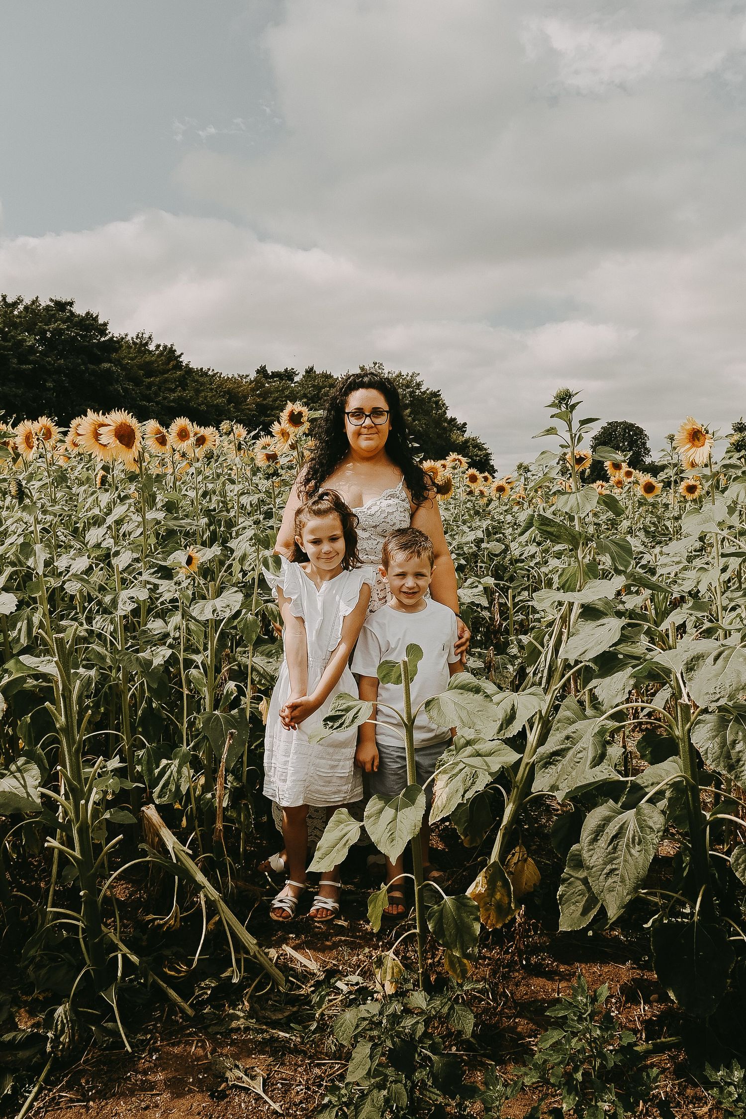 Children exploring a vibrant sunflower field on a cloudy day.