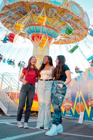 Friends enjoying a colorful carnival with a spinning swing ride in the background.