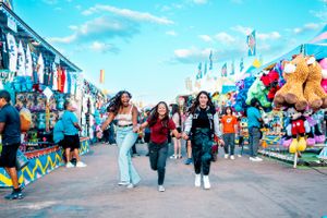 Friends running excitedly through a carnival midway filled with games and prizes.