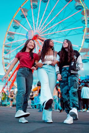 Friends walking together at a carnival with a ferris wheel in the background.