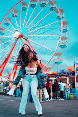 Two friends having fun posing in front of a towering ferris wheel at a carnival.
