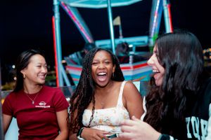 Three friends share a genuine moment of laughter at a nighttime carnival.