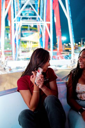 Friends sharing joyful conversation with carnival rides illuminated in background.