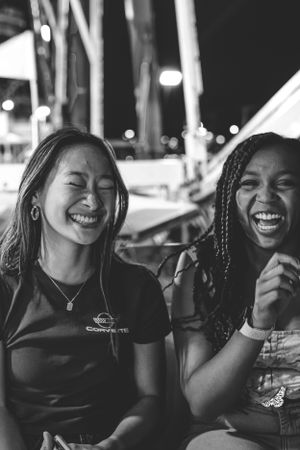Two friends share authentic laughter while enjoying an evening at a carnival.