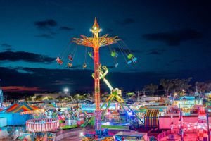 Illuminated carnival rides and attractions create a colorful nighttime display against dark blue sky.