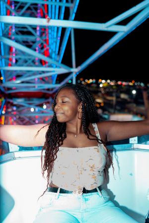 Woman spreads arms joyfully against blue-lit carnival ride structure at night.