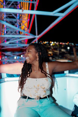 Person enjoying carnival atmosphere with arms spread wide against illuminated ride structure.