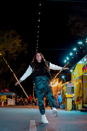 Person jumping with arms outstretched under carnival string lights at night.