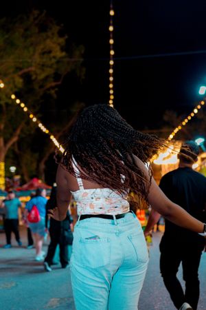 Back view of person with braided hair enjoying carnival atmosphere under string lights.