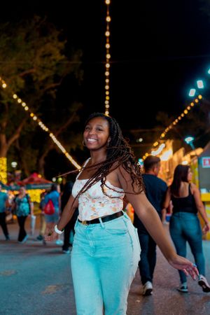Person in turquoise jeans and floral top enjoying a festive carnival evening.