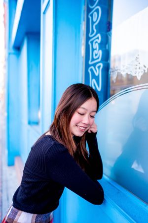 Person in black sweater leans against blue storefront window.