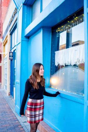 Person in plaid skirt looks through blue-framed storefront window.