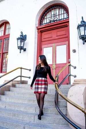 Stylish plaid skirt outfit on steps of historic building with red door and vintage lanterns.