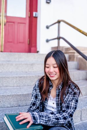 Person relaxing with book on steps near red door entrance.