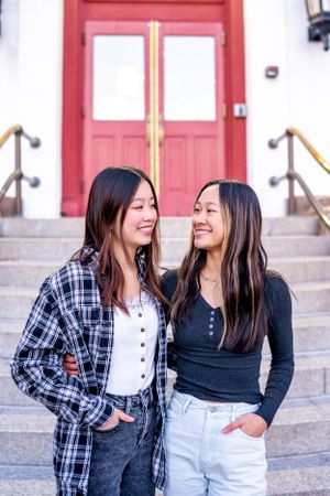 Two friends sharing a laugh on stone steps with red door entrance.