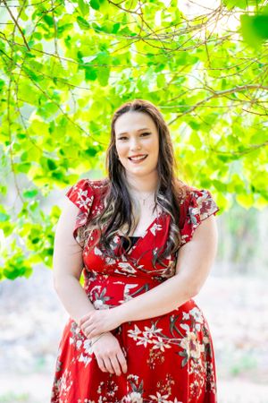 Portrait in red floral dress against lush green foliage background.