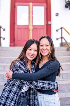 Friends embracing and smiling on steps of building entrance.