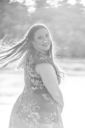 Black and white portrait of graduate in floral dress with hair flowing in breeze.