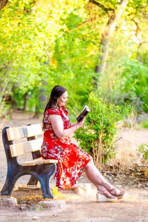 Graduate reads book while relaxing on wooden bench in park setting.