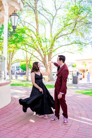 A couple dances together on brick pavement, one in a burgundy suit and the other in a flowing black dress.
