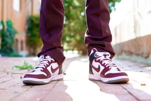 Burgundy and white Nike sneakers shown on brick pavement with matching burgundy pants.