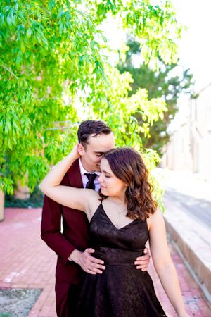 A romantic moment between a couple in formal wear under green leafy trees.